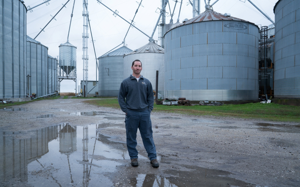 Man stands in front of grain bins.